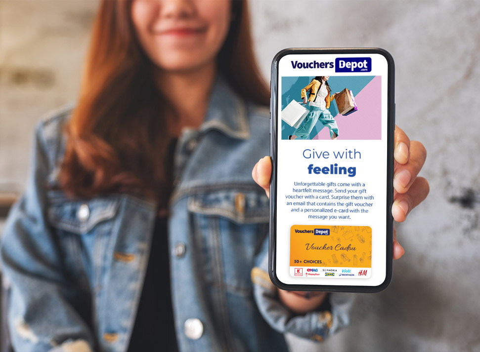 Femeie zâmbitoare ține în mână un smartphone care afișează site-ul Vouchers Depot și mesajul „Give with feeling” – platformă online de carduri cadou digitale pentru orice ocazie.